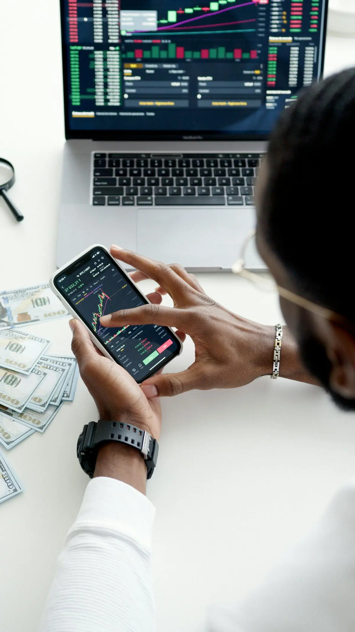 A person checking financial data on a smartphone and laptop