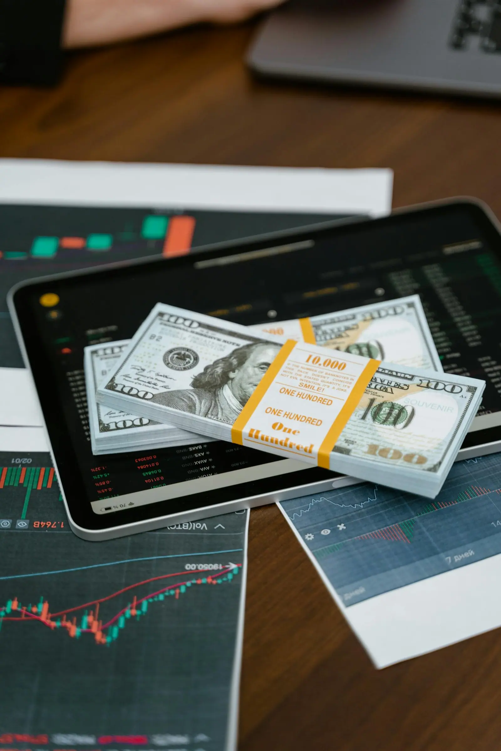 Banknotes resting on a tablet displaying financial graphs