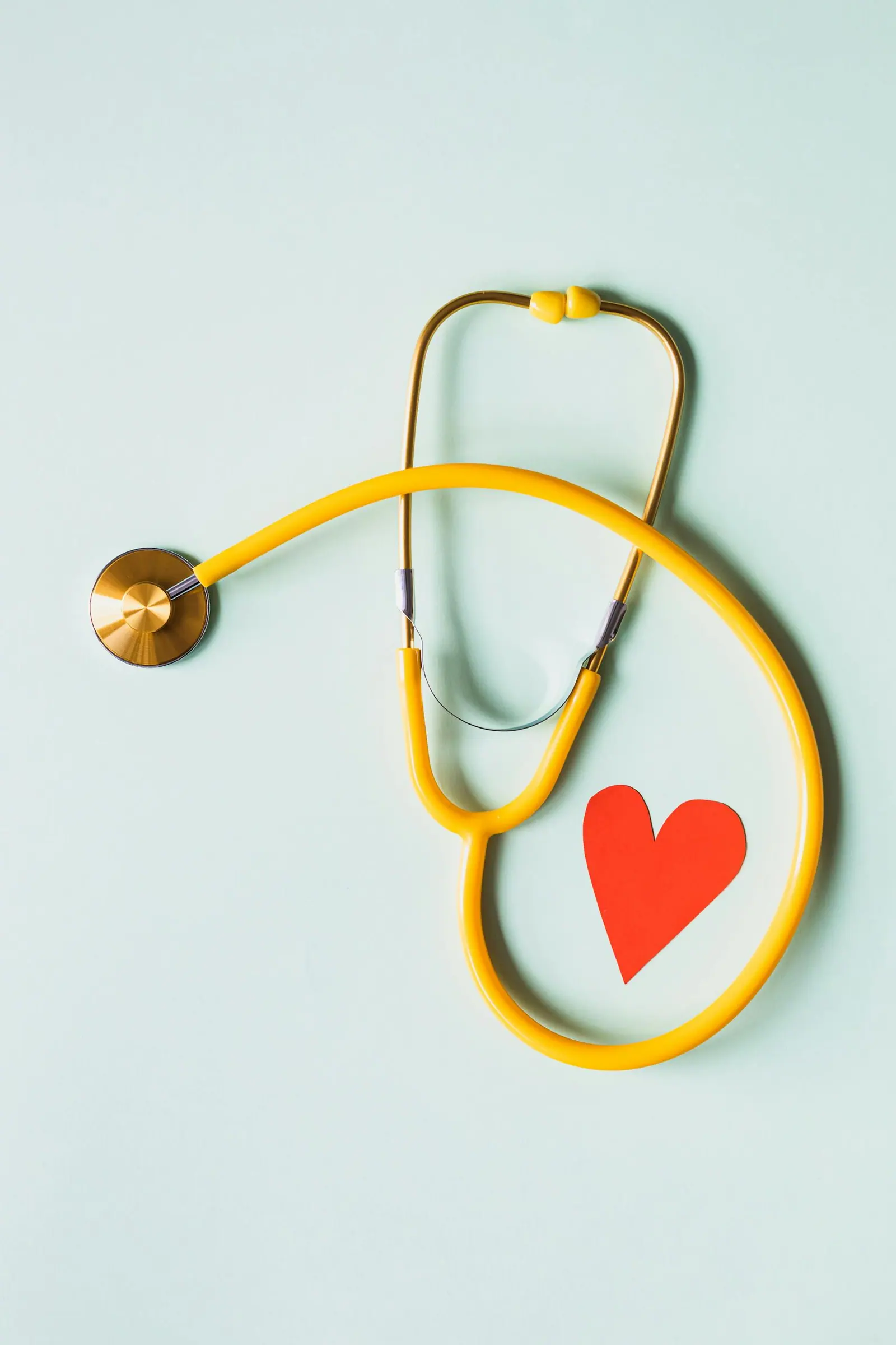 A stethoscope arranged with a paper heart on a light green background