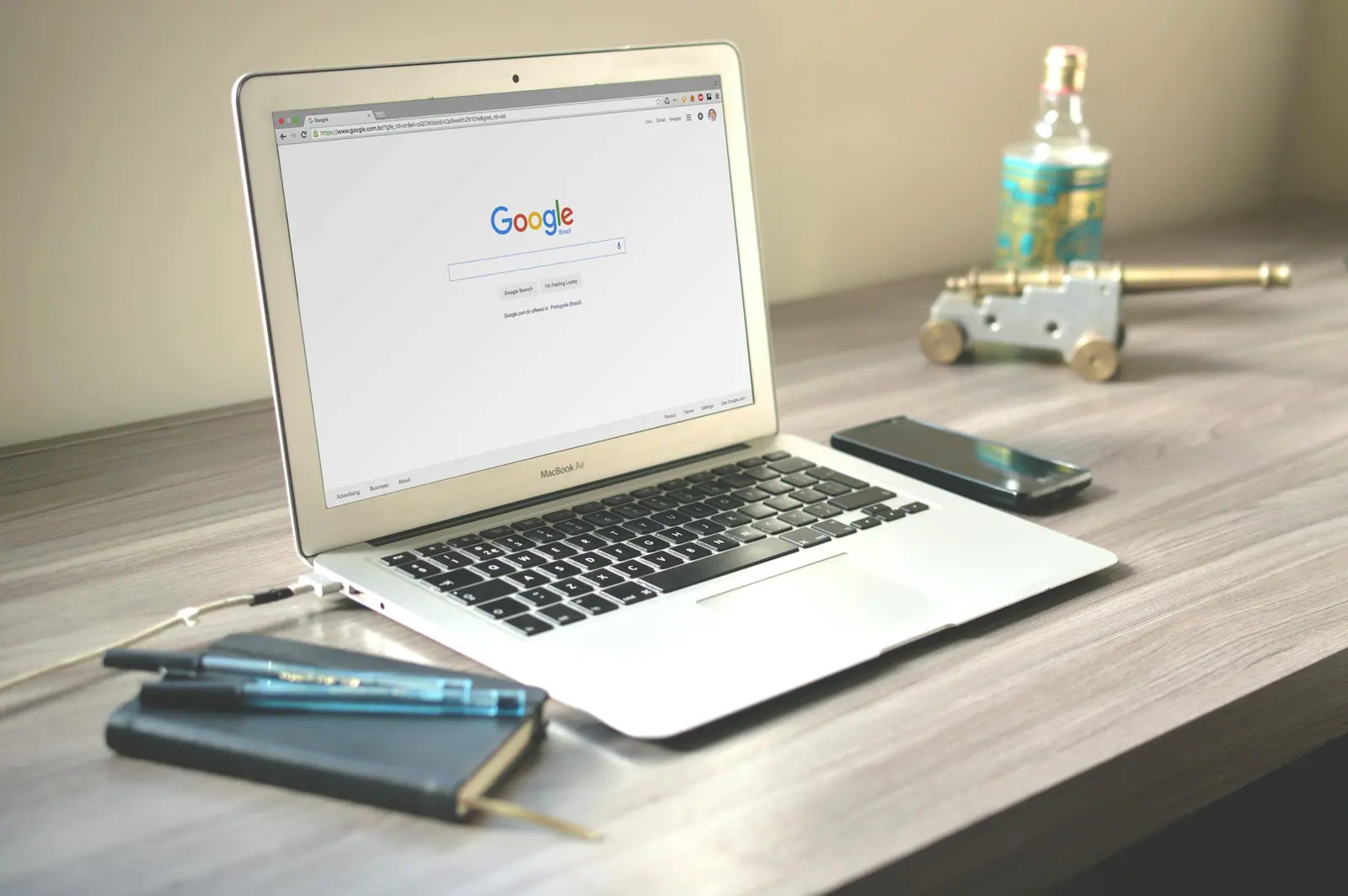 A neat workspace featuring a laptop displaying google search a smartphone and a notebook on a wooden desk