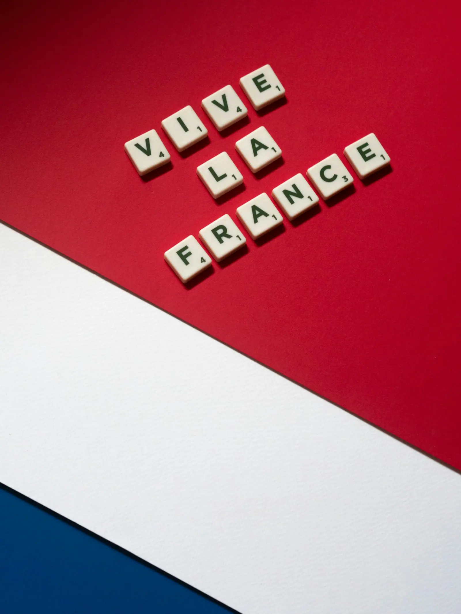Scrabble tiles spelling 'Vive La France' on a French flag background convey national pride.